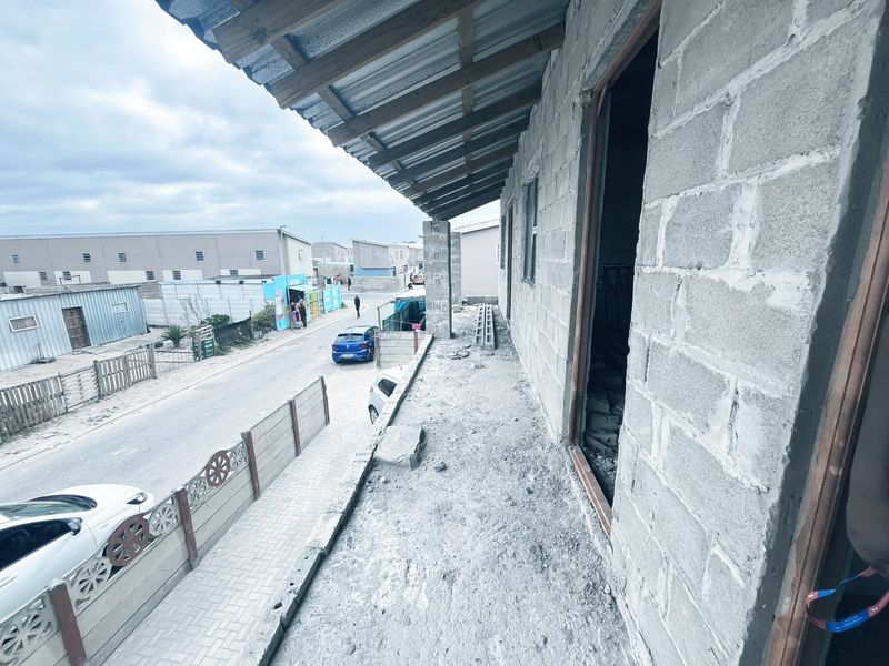 An unfinished exterior balcony area featuring exposed concrete block walls and a corrugated metal roof, offering a view over the street.