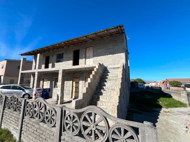 Two-story residential property under construction featuring exposed concrete block walls, an external staircase, and a corrugated metal roof.