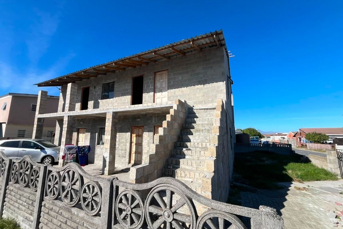 Two-story residential property under construction featuring exposed concrete block walls, an external staircase, and a corrugated metal roof.