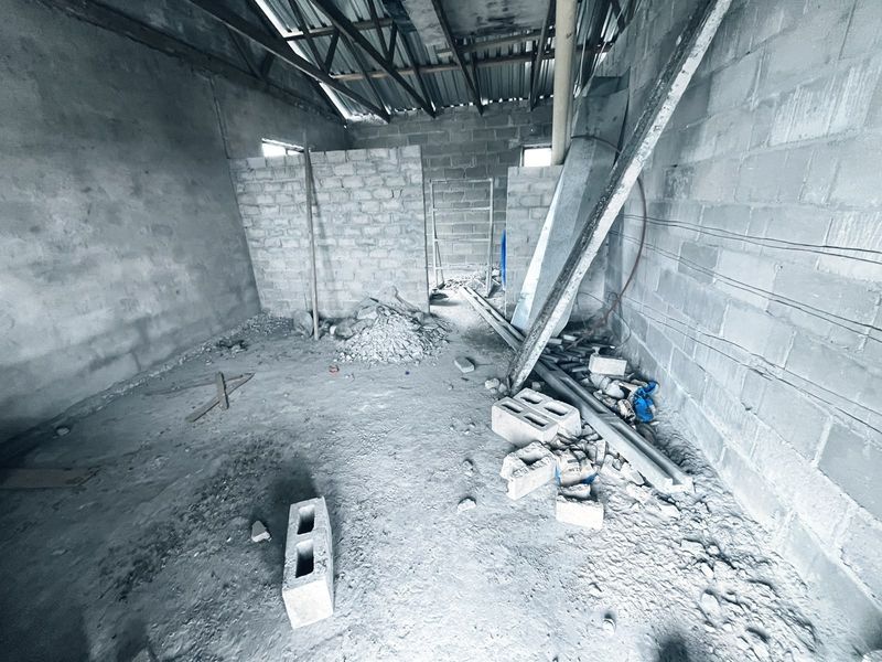 An unfinished interior space featuring exposed concrete block walls, exposed roof trusses, and a raw concrete floor, currently in a shell construction state.