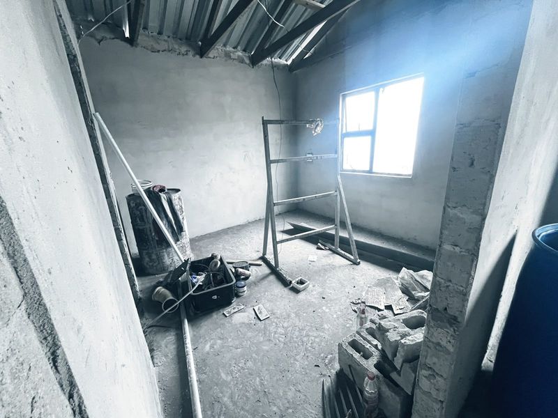 An unfinished room in shell condition featuring exposed roof trusses, plastered walls, and a cement screed floor, awaiting final finishes and flooring installation.
