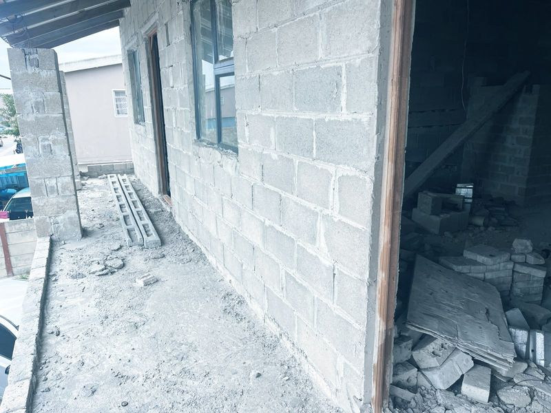 An unfinished exterior view of a property under construction, featuring exposed concrete block walls, aluminum window frames, and a concrete slab walkway.