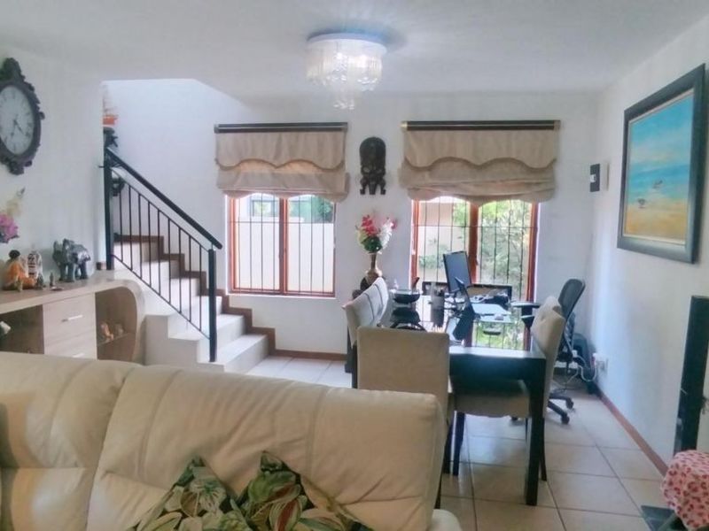 Open plan living area featuring tiled flooring, a staircase with a metal balustrade, and windows fitted with security bars.