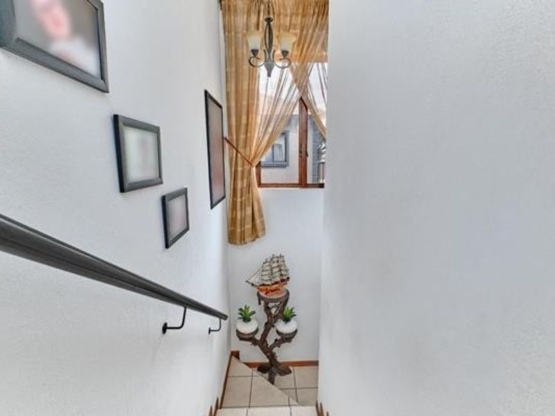 A bright hallway featuring a staircase with a handrail, a window with curtains, and a ceiling light fixture.