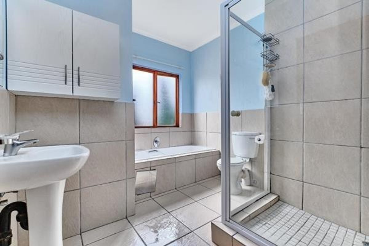 A functional bathroom featuring a pedestal basin, built-in bathtub, separate shower enclosure, and wall-mounted storage cabinetry with tiled finishes throughout.