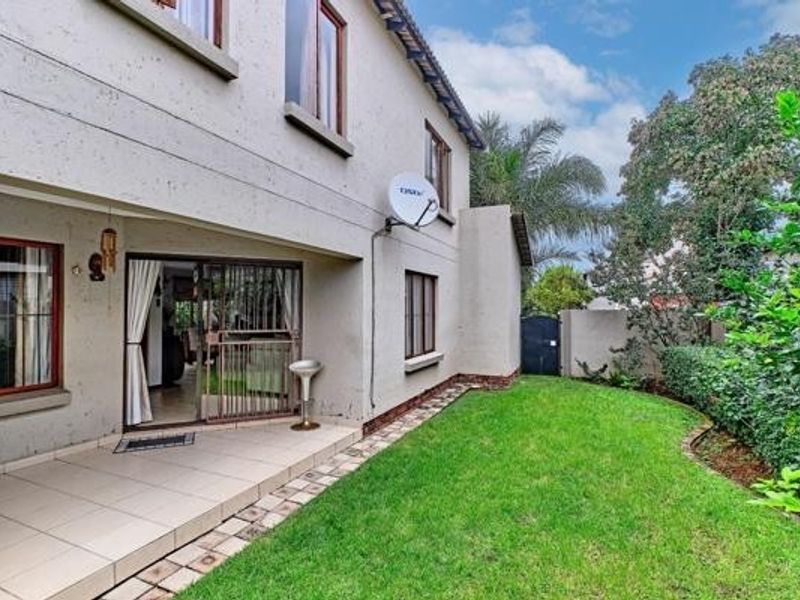 Rear view of the property featuring a tiled patio area, sliding glass doors, and a well-maintained lawn with established garden hedging.
