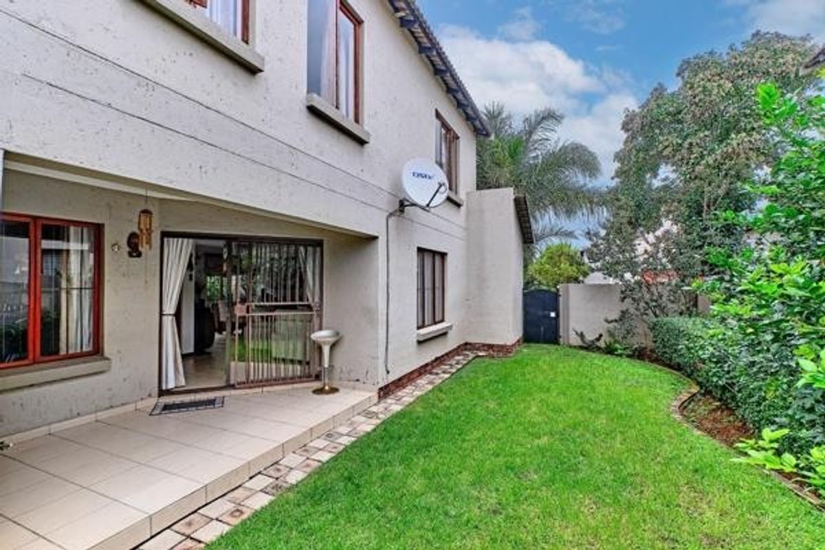 Rear view of the property featuring a tiled patio area, sliding glass doors, and a well-maintained lawn with established garden hedging.
