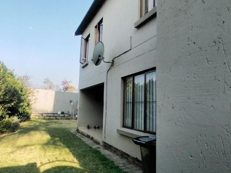 Rear view of the property showing the exterior facade, paved walkway, and garden area with boundary wall.