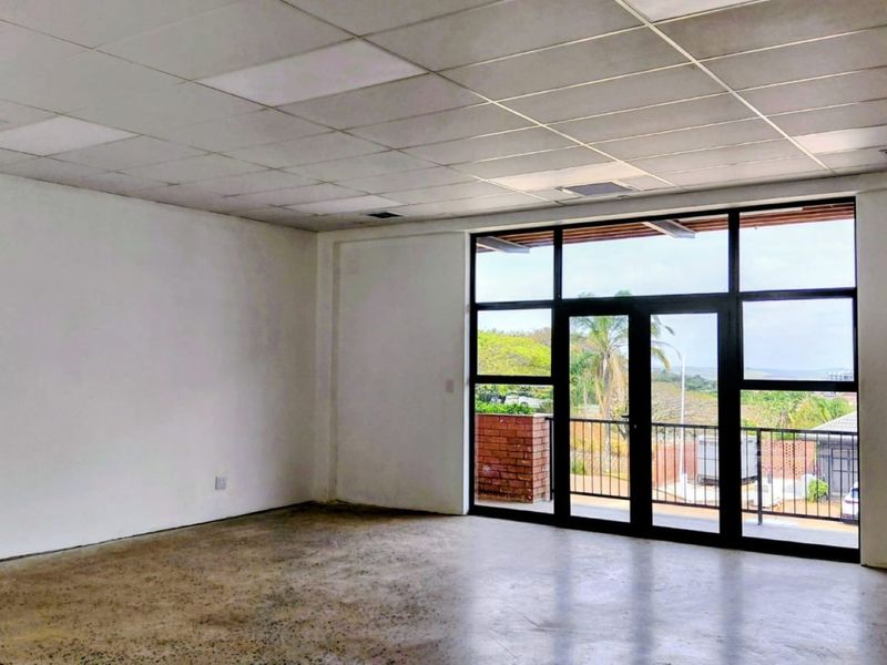 Spacious, empty office area featuring a polished concrete floor, suspended ceiling, and large glass doors leading to an outdoor balcony.