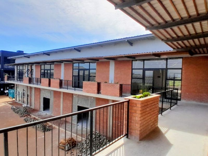 An exterior view of a modern office building featuring exposed brickwork, a covered balcony with metal railings, and large glass windows.
