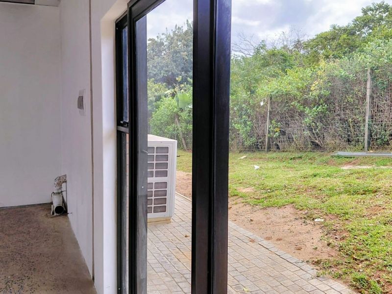 Empty office space featuring exposed concrete floors and a sliding glass door opening onto a private paved patio and garden area.
