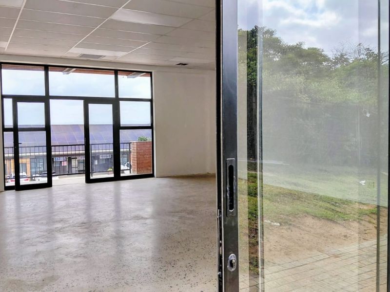 Spacious, modern office area featuring polished concrete flooring, a suspended ceiling, and large glass doors providing ample natural light and outdoor access.