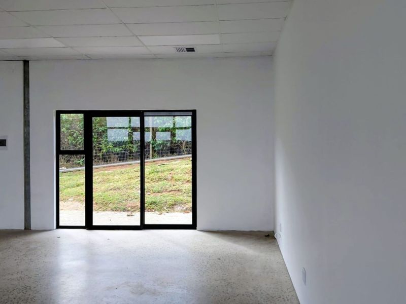 A bright, empty office space featuring a polished concrete floor, suspended ceiling, and a large sliding glass door providing natural light and garden views.