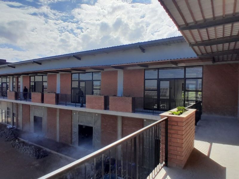 A view of the office building exterior featuring exposed brickwork, a covered balcony with metal railings, and large glass windows.