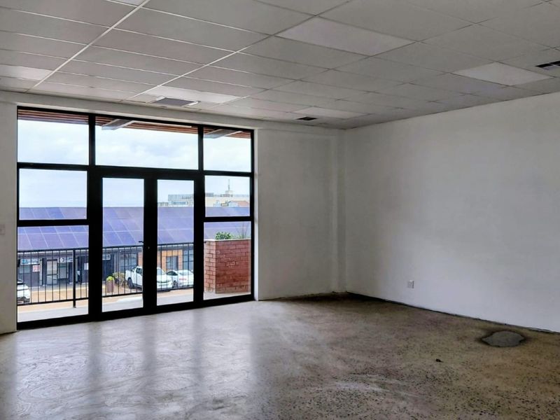A spacious, empty office unit featuring a polished concrete floor, suspended ceiling, and large glass doors providing natural light and exterior views.