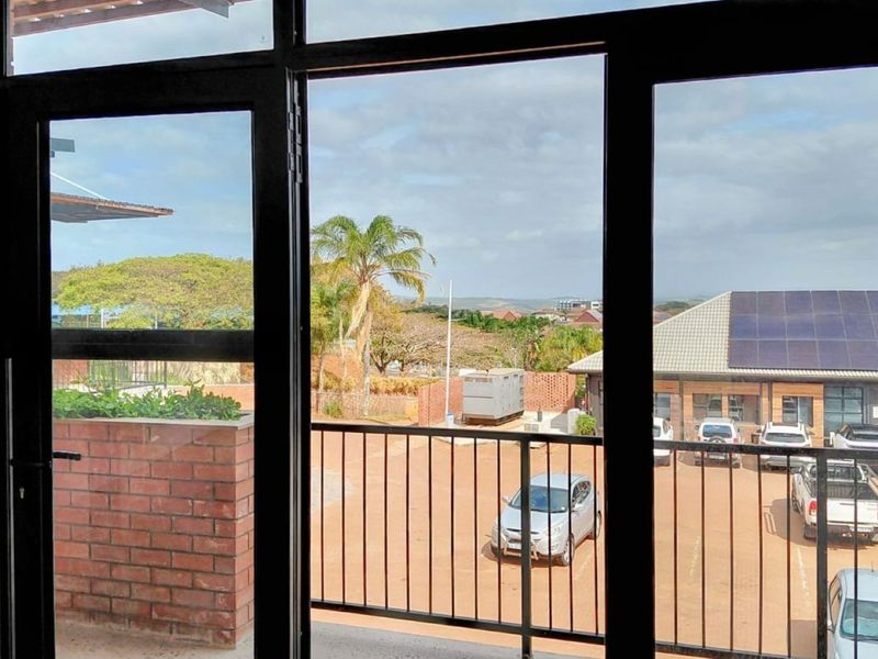 View from an office space looking out over a parking area and surrounding landscape through large black aluminium framed windows.