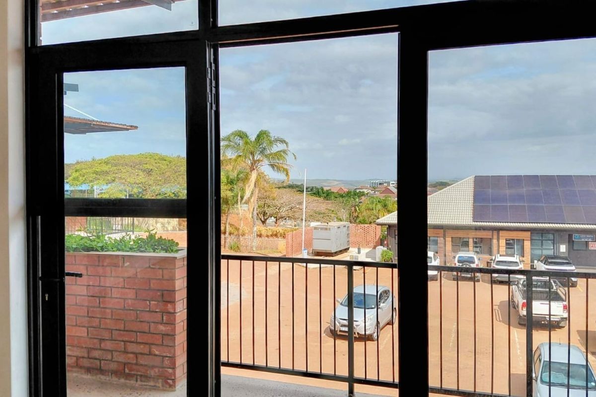 View from an office space looking out over a parking area and surrounding landscape through large black aluminium framed windows.