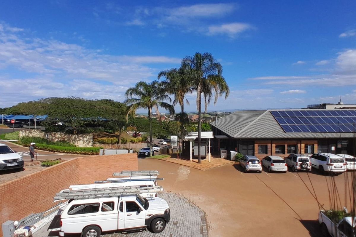Aerial view of the office property featuring a large parking area, brick boundary walls, and a building roof equipped with solar panels.