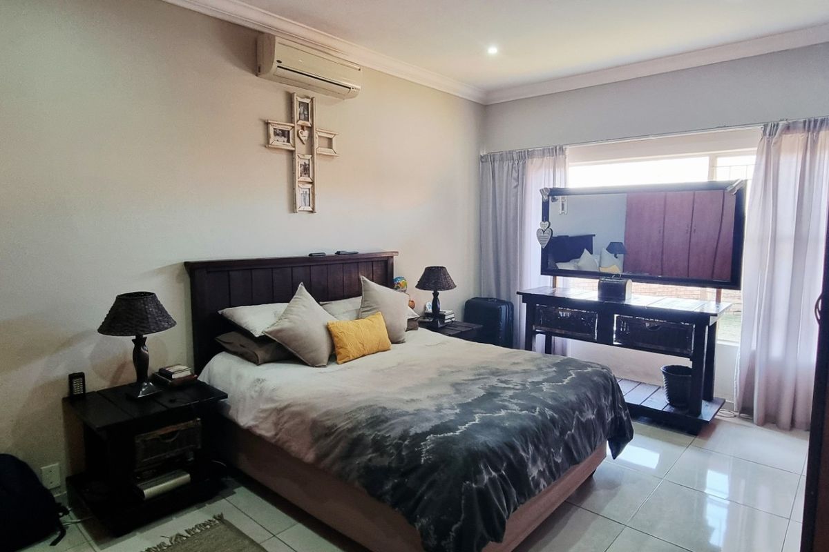 A spacious bedroom featuring tiled flooring, a wall-mounted air conditioning unit, and large windows that provide natural light.