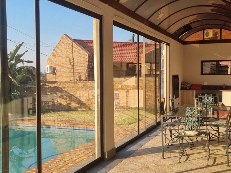 A spacious covered patio featuring tiled flooring, built-in cabinetry with a sink, and large sliding glass doors overlooking the swimming pool and garden.