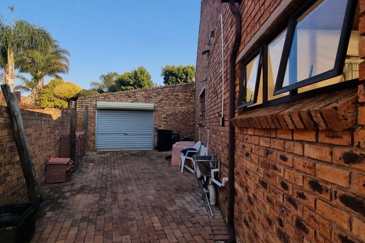 Rear exterior area featuring brick paving, a boundary wall, a garage roller door, and an external utility sink.