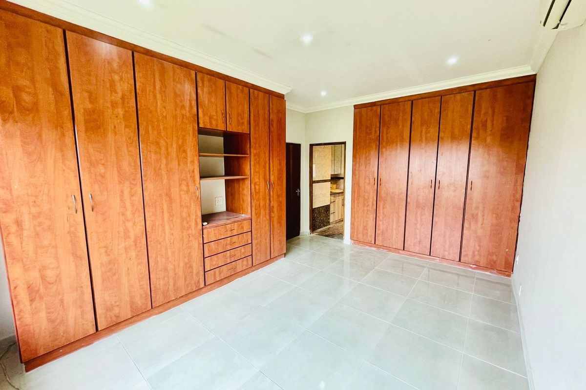 Spacious bedroom featuring extensive built-in wooden cabinetry, neutral tiled flooring, recessed lighting, and an integrated air conditioning unit.