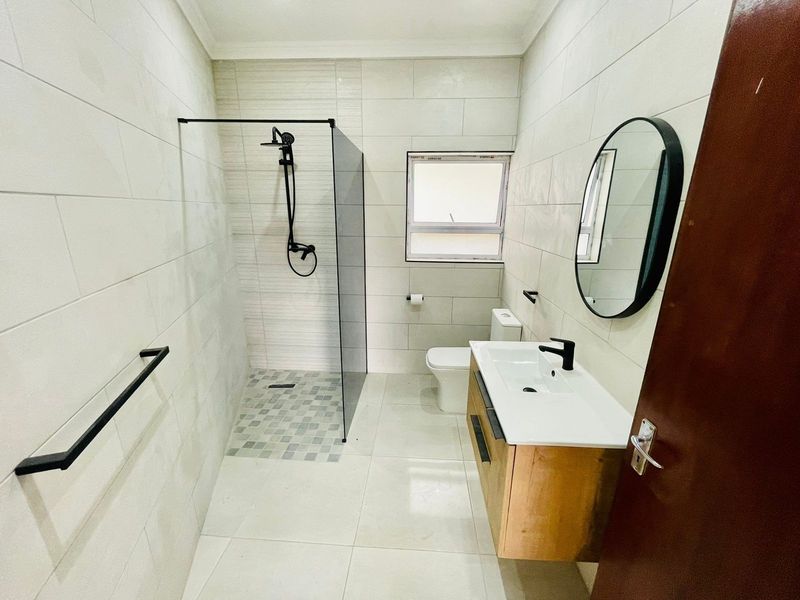 Modern bathroom featuring a walk-in shower with black fixtures, a floating vanity cabinet, and contemporary wall and floor tiling.