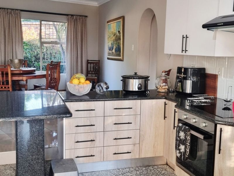 Open-plan kitchen and dining area featuring modern cabinetry, granite countertops, built-in appliances, and direct access to the garden through sliding glass doors.