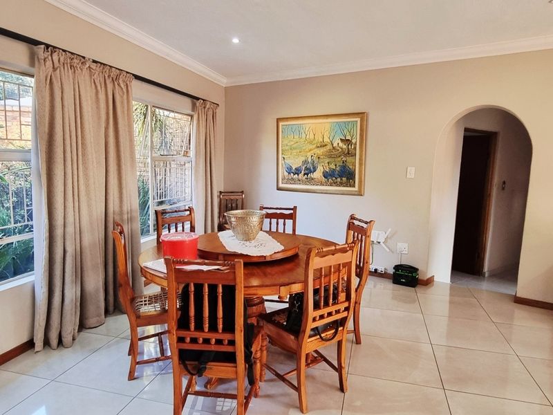 A bright dining room featuring large windows, tiled flooring, and a classic archway leading to an adjacent space.
