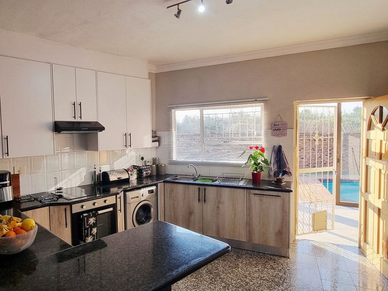 Modern kitchen featuring white and wood-grain cabinetry, granite countertops, built-in appliances, and direct access to the outdoor pool area.