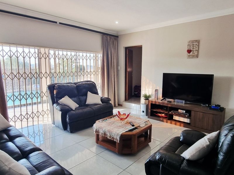 A bright living room featuring large sliding glass doors with security gates, tiled flooring, and recessed ceiling lighting.
