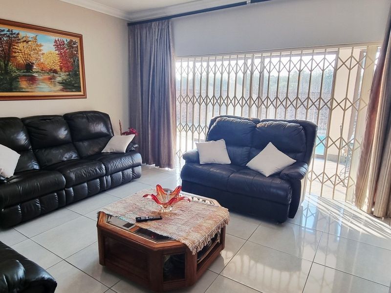 A well-maintained living room featuring neutral tiled flooring, coving, and a large security gate providing access to the outdoor area.