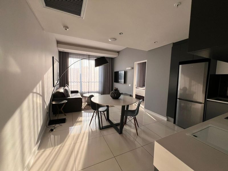 Modern open-plan living and kitchen area featuring sleek tiled floors, recessed lighting, and integrated cabinetry, with direct access to a balcony.