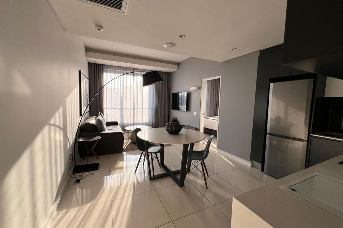 Modern open-plan living and kitchen area featuring sleek tiled floors, recessed lighting, and integrated cabinetry, with direct access to a balcony.