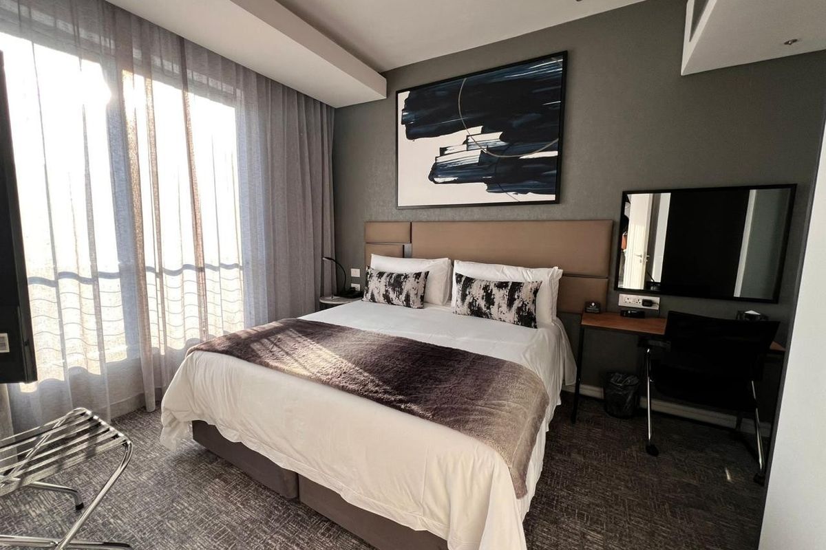A well-maintained bedroom featuring a built-in headboard, recessed ceiling lighting, and large windows with floor-to-ceiling curtains, creating a comfortable and modern living space.