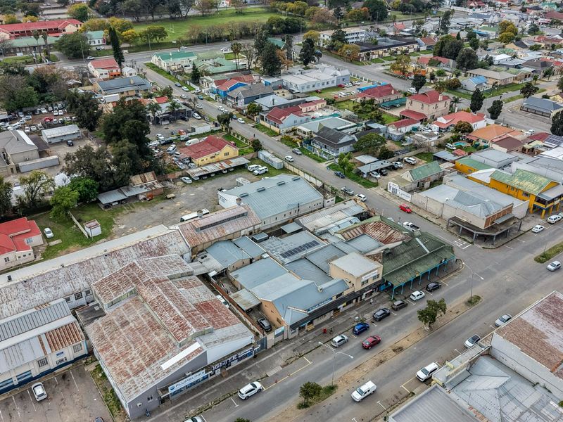 Aerial view of a commercial property complex featuring multiple buildings with corrugated metal roofing and adjacent asphalt parking areas in an urban setting.