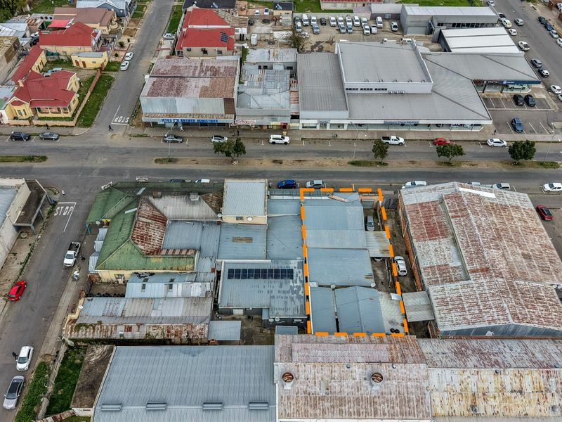 Aerial view of a commercial property block featuring corrugated metal roofing, solar panel installations, and surrounding street infrastructure in an urban setting.