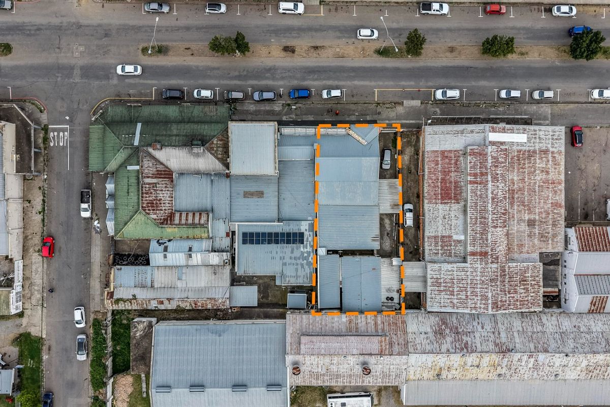 Aerial view of the property showing the building footprint, corrugated metal roof structure with solar panels, and adjacent street parking.
