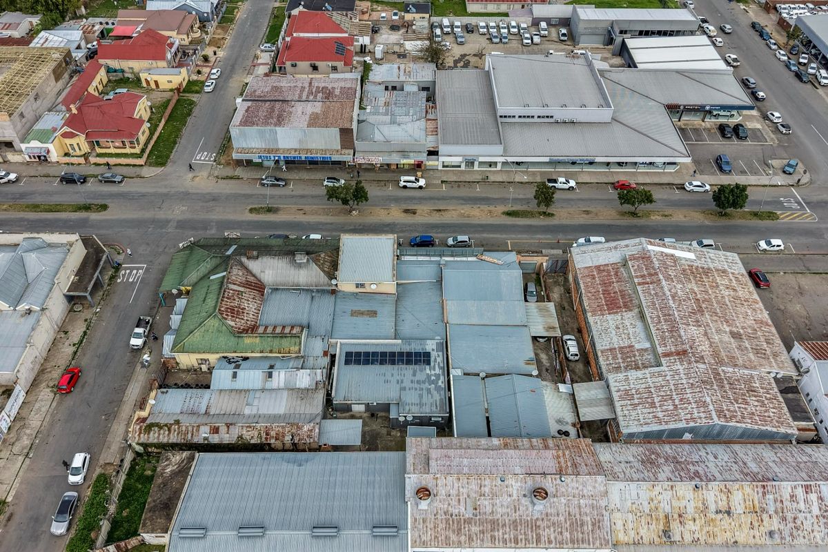 Aerial view of a commercial property complex featuring multiple corrugated metal roof sections, solar panel installations, and adjacent street-level parking.