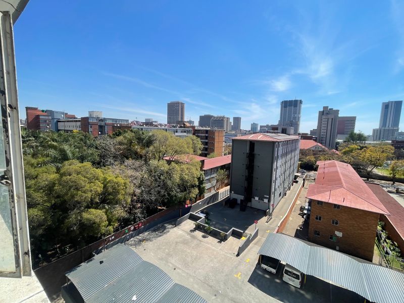 An elevated urban view overlooking surrounding apartment buildings, parking areas, and mature trees under a clear blue sky.