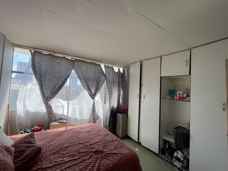 A bedroom featuring built-in cupboards and a large window providing natural light. The space requires cosmetic updates to improve its overall condition.