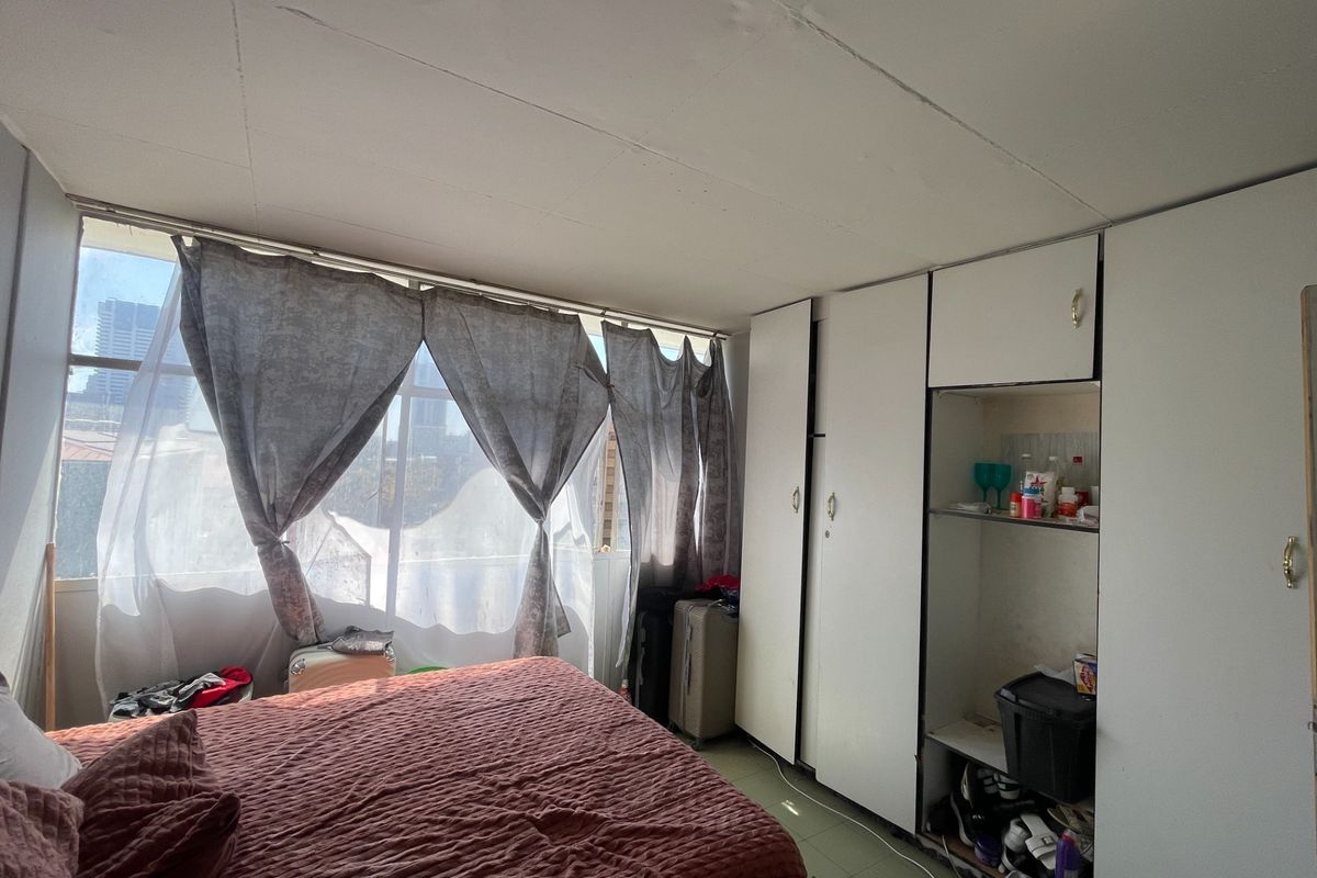 A bedroom featuring built-in cupboards and a large window providing natural light. The space requires cosmetic updates to improve its overall condition.
