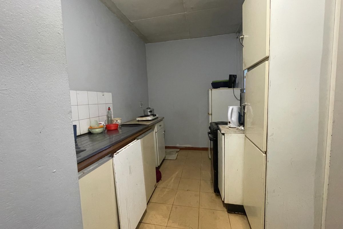A dated kitchen featuring basic cabinetry, tiled flooring, and a stainless steel sink, offering significant potential for modernization and renovation.