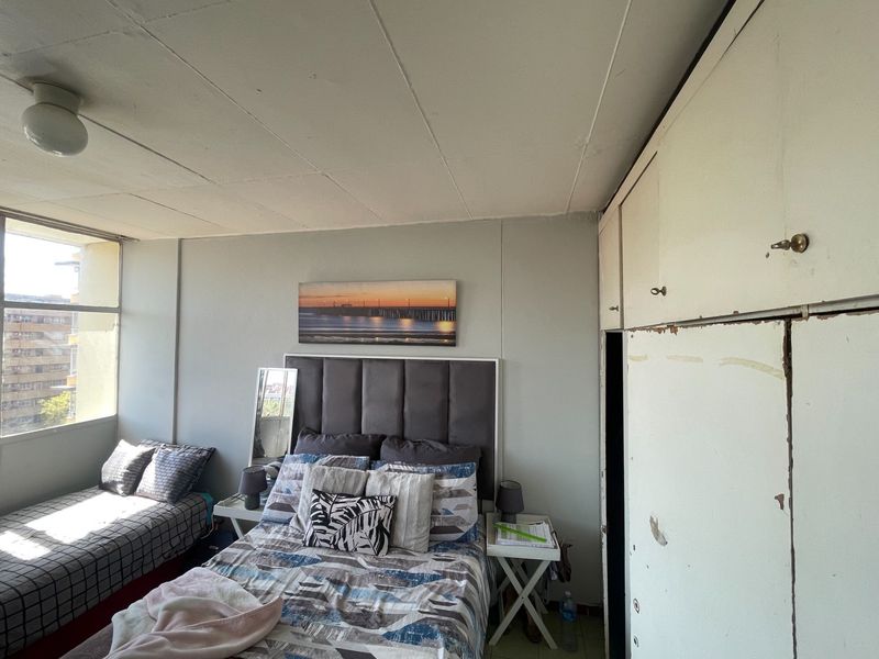 Bedroom featuring built-in cupboards and a large window, providing natural light. The room requires cosmetic updates to the cabinetry and finishes.