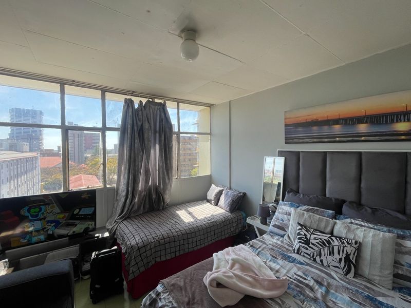 A bedroom featuring large steel-framed windows with city views and a ceiling-mounted light fixture.