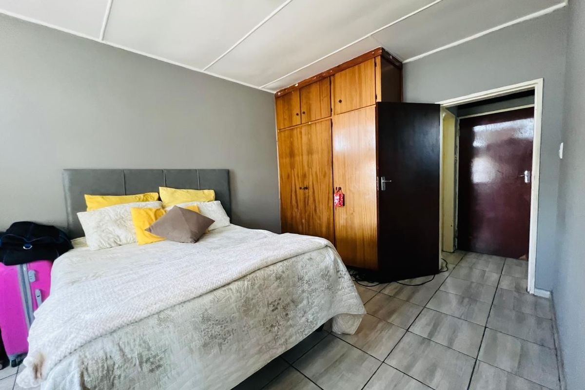A bedroom featuring tiled flooring, a built-in wooden wardrobe, and a panelled ceiling.