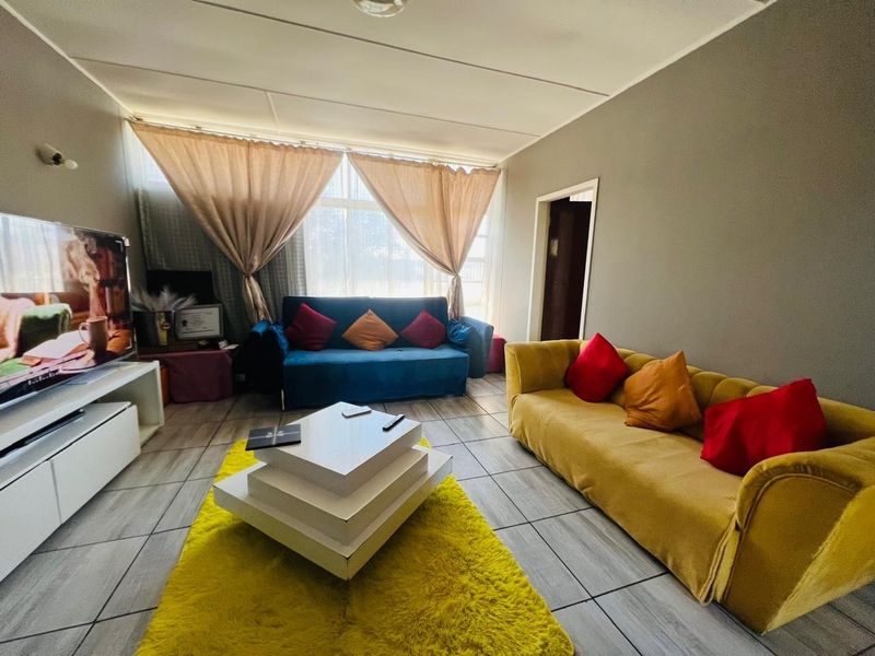 A living room featuring tiled flooring, large windows allowing natural light, and neutral wall finishes.