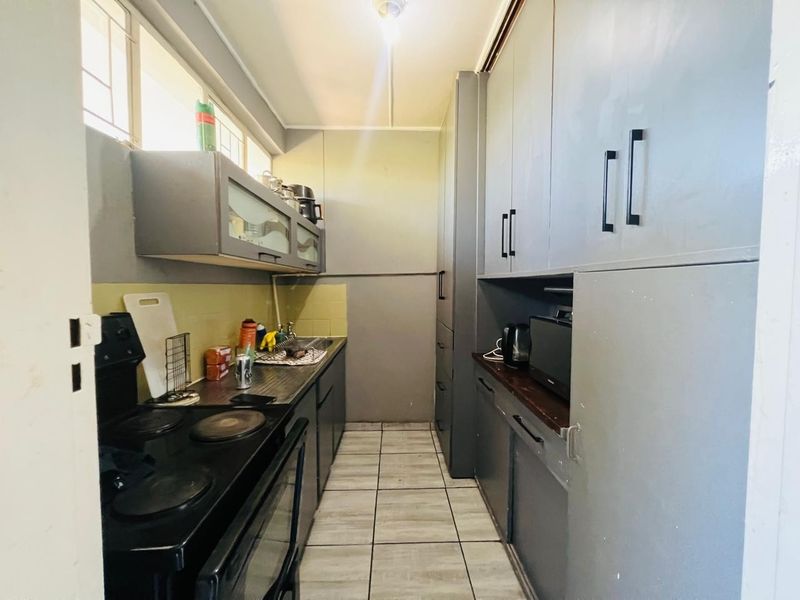 A functional galley-style kitchen featuring built-in cabinetry, tiled flooring, and a tiled backsplash with an integrated electric stove.