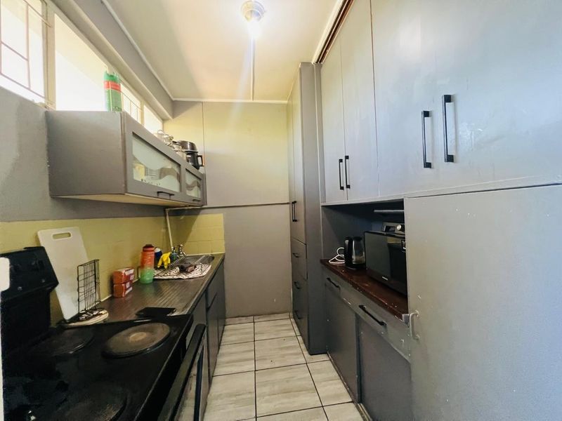 A compact kitchen featuring built-in cabinetry, tiled flooring, a sink, and an electric stove with a tiled backsplash.