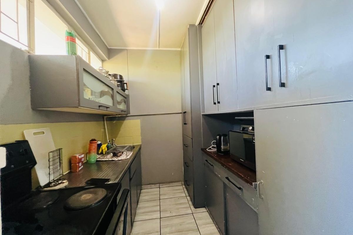 A compact kitchen featuring built-in cabinetry, tiled flooring, a sink, and an electric stove with a tiled backsplash.